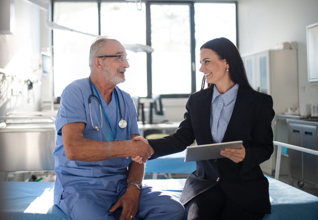 Young business woman shaking hand with elderly doctor in a hospital room.