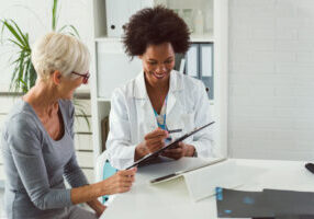 A female doctor sits at her desk and chats to an elderly female
