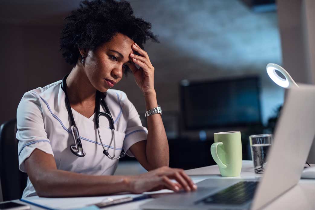 stressed provider about health system bad debt at computer and desk with head in hand